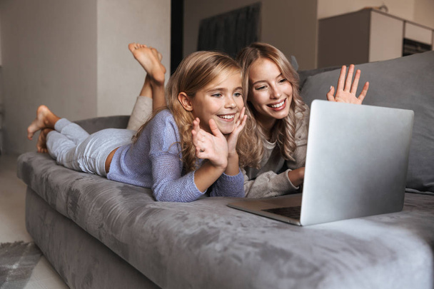 Young woman with her little sister indoors at home using laptop computer. - 写真・画像