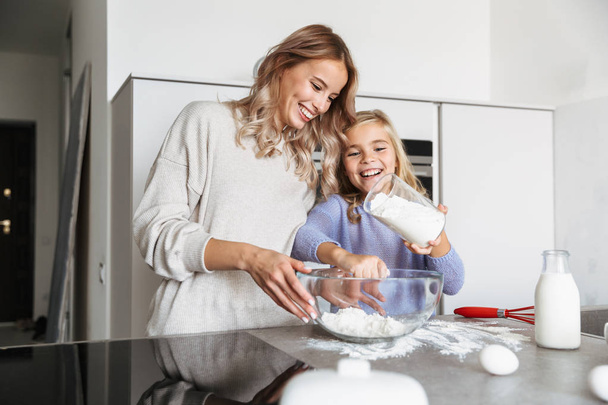 Woman with her little sister indoors at home kitchen cooking with flour. - Φωτογραφία, εικόνα