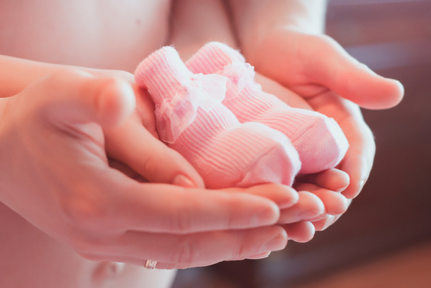 руки мужчины и женщины (отца и матери) с розовыми детскими ботинками. Концепция беременности и ожидания ребенка
 - Фото, изображение