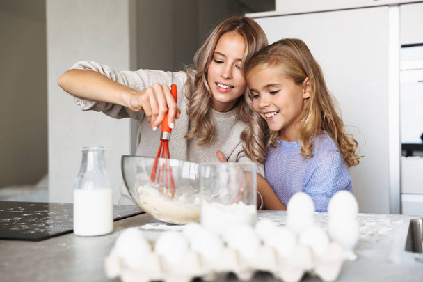 Szczęśliwa młoda kobieta z jej siostra pomieszczeniu w domowej kuchni do gotowania z mąki i jajka z mlekiem. - Zdjęcie, obraz
