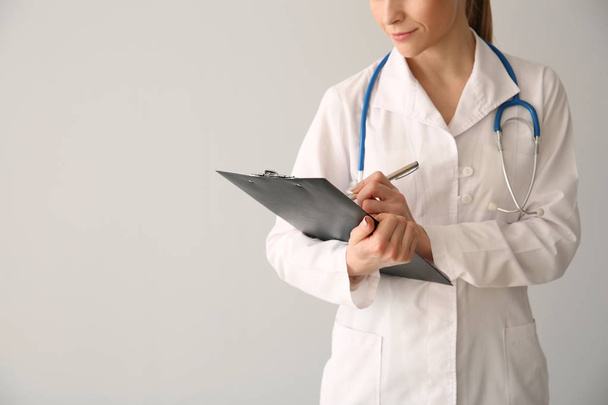Female doctor with clipboard on light background - Foto, afbeelding
