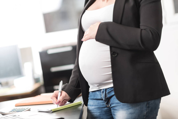 Беременная женщина делает заметки в офисе
 - Фото, изображение