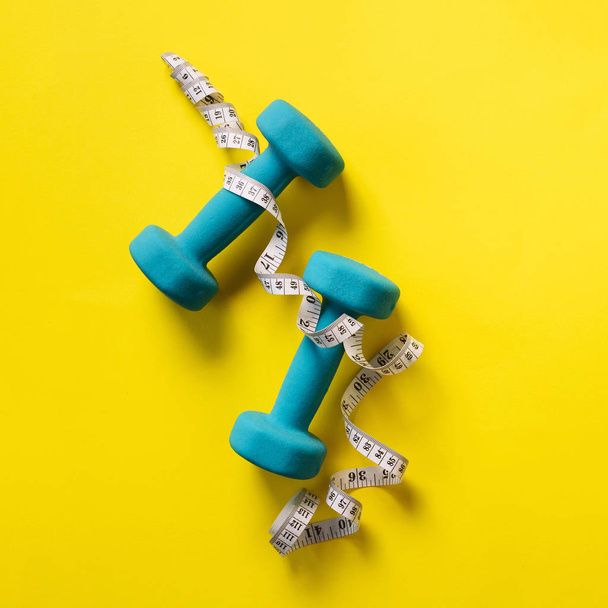 Fitness, sport concept with dumbbells and measuring tape over yellow background. Banner, copy space. Top view. Flat lay. Square crop - Fotoğraf, Görsel