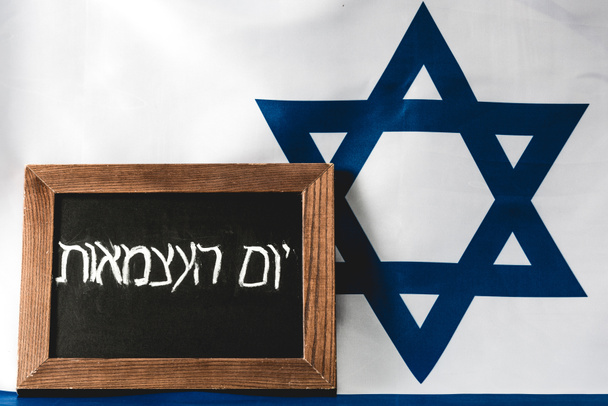 chalkboard with hebrew lettering near blue star of david on national flag of israel  - Fotó, kép