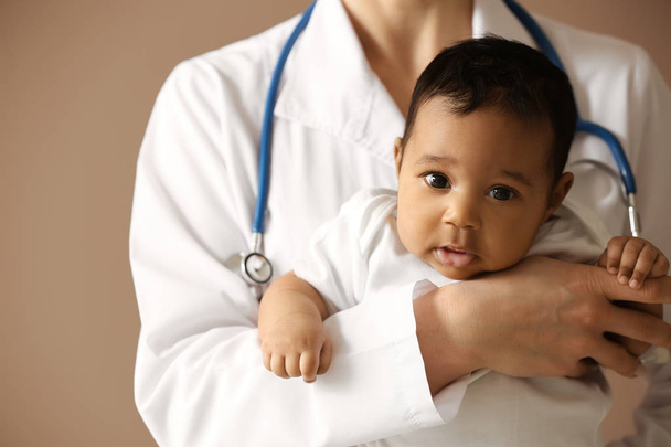 Pediatrician with African-American baby on color background - Foto, Imagen