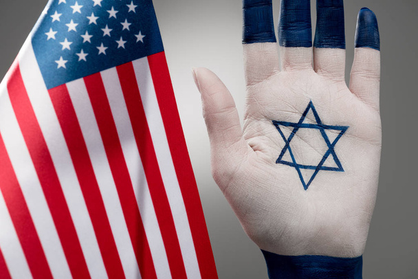 selective focus of female hand with jewish star of david near american flag on grey  - Photo, Image