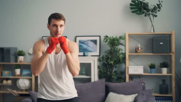 Young man boxer in sportswear training at home boxing alone with wrapped wrists - Video