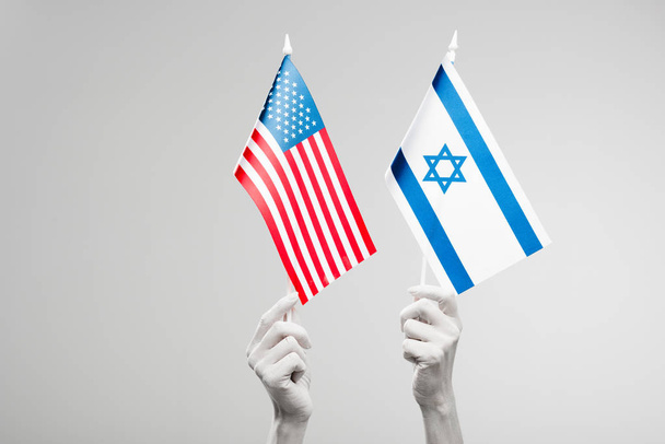cropped view of female hands painted in white holding american and israel flags isolated on grey  - Photo, image