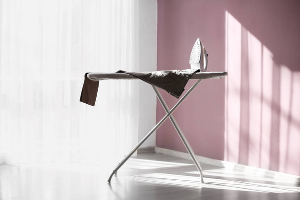 Ironing board with clean clothes in room - Foto, imagen