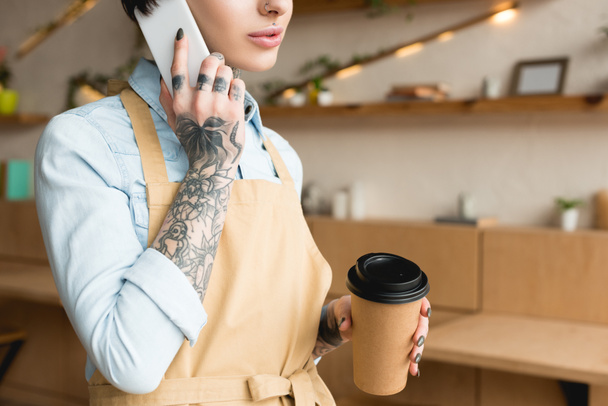 cropped view of waitress talking on smartphone and holding disposable cup - Photo, Image