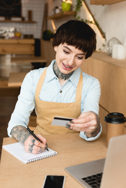 smiling waitress looking at credit card and writing in notebook - Фото, зображення