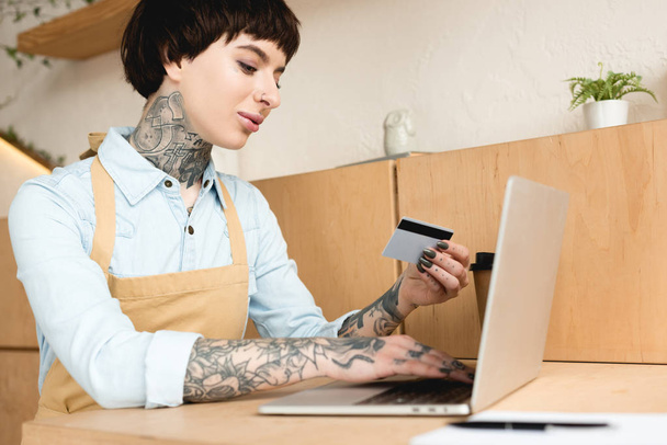 atraktivní servírka při pohledu na kreditní karty a psaní v poznámkovém bloku - Fotografie, Obrázek