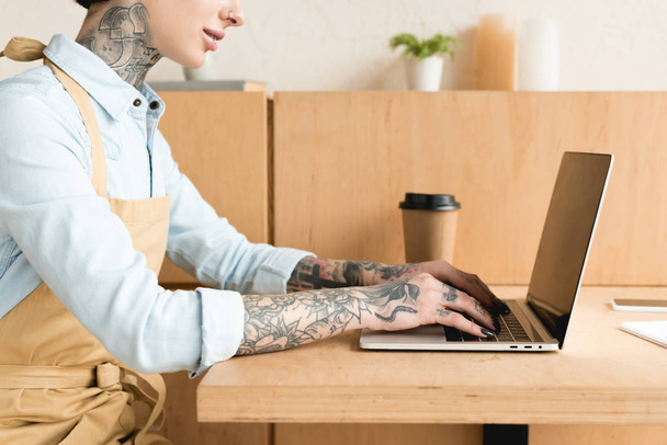 vista parziale della cameriera utilizzando il computer portatile mentre seduto a tavola vicino alla tazza di carta
 - Foto, immagini