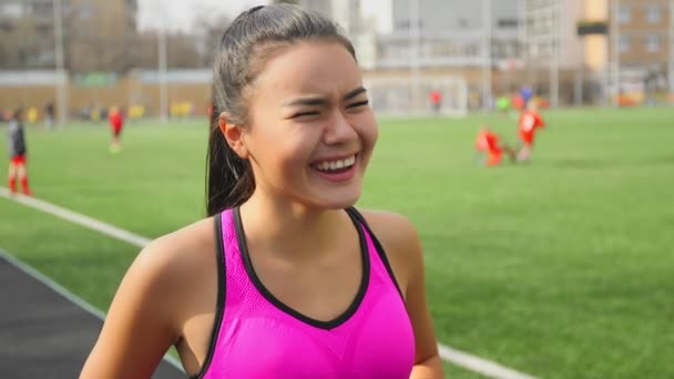 Портрет азиатской бегуньи, смеющейся на стадионе перед стартом
. - Кадры, видео