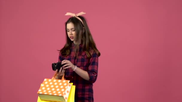 Girl looks into shopping bags then the purse has run out of money but there is a card. Pink background. Slow motion - Imágenes, Vídeo