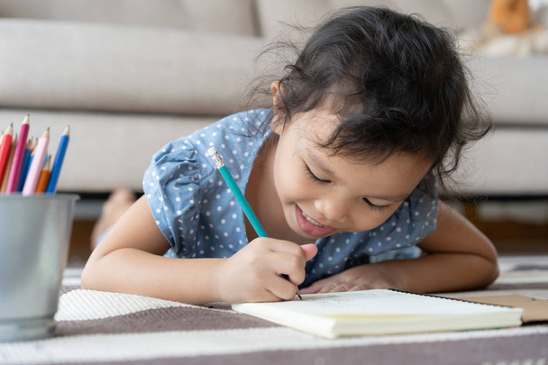 Милая маленькая девочка рисует домашнее задание и пишет ручкой на бумаге в своем доме
 - Фото, изображение