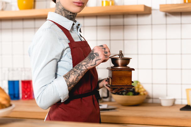 partial view of tattooed barista in apron holding coffee grinder - Photo, Image