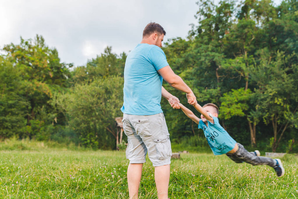 Mies pyörittää poikaa vihreällä kentällä. leikkimistä
 - Valokuva, kuva