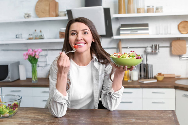 Beautiful woman eating healthy salad in kitchen at home - Photo, Image