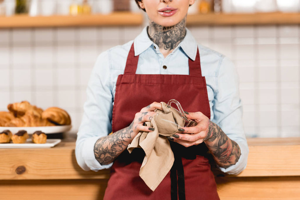 partial view of barista in apron wiping glass cup with rag   - Photo, Image