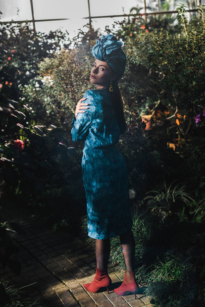 Full length view of attractive woman in blue dress and turban in orangery - Photo, image