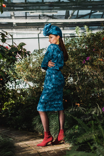 Ganzkörperansicht der attraktiven Frau in blauem Kleid und Turban in der Orangerie - Foto, Bild