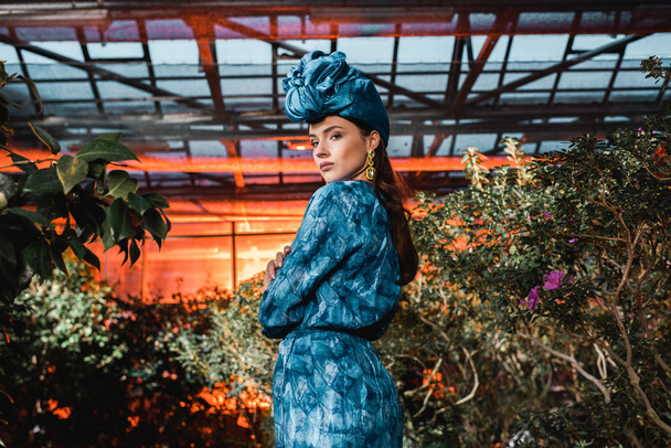 Gorgeous young woman in blue dress in turban in orangery - 写真・画像