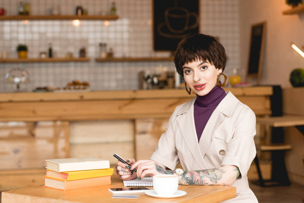 atraente, mulher de negócios confiante sentado na cafetaria e olhando para a câmera
 - Foto, Imagem