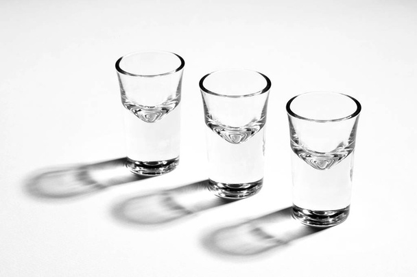 Monochrome image of three empty shot glasses, back lit, with hard reflections - Foto, Imagem