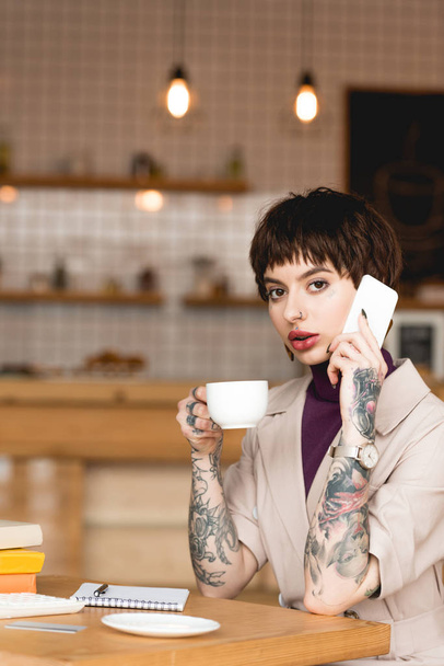 attractive businesswoman talking on smartphone, holding coffee cup and looking at camera - Foto, immagini