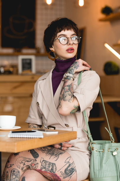 beautiful, fashionable businesswoman in eyeglasses holding bag and looking away - Фото, изображение