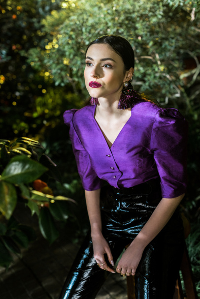 Pensive woman in purple blouse stting on chair in botanical garden - Photo, Image