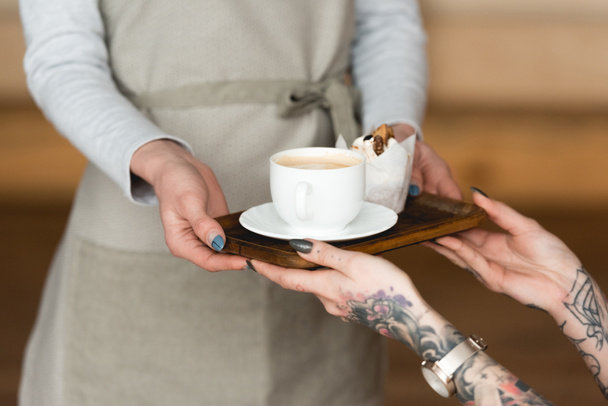 vista parcial de mujer de negocios tatuada tomando bandeja con taza de café y pastel de camarera
  - Foto, imagen