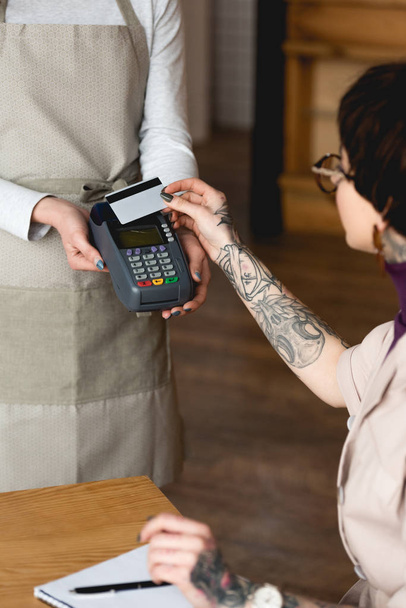 selective focus of businesswoman holding credit card near waitress with payment terminal - Fotografie, Obrázek