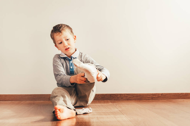 Niño con mucha independencia sentado en el suelo poniéndose
  - Foto, Imagen