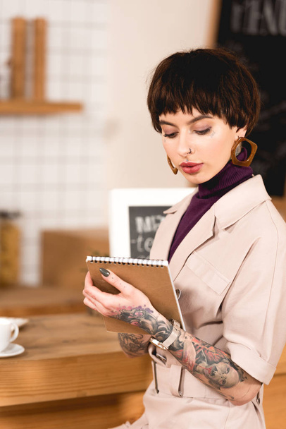 fashionable businesswoman holding notebook while standing at bar counter in cafe - Foto, immagini