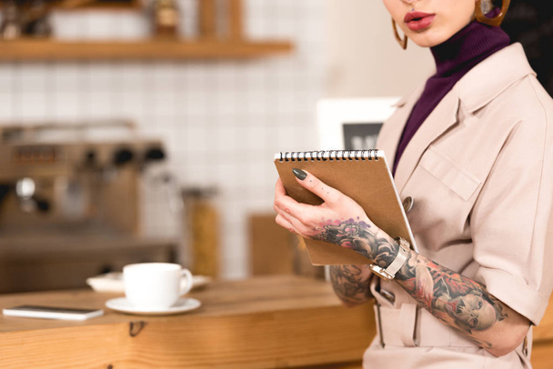 partial view of businesswoman holding notebook while standing at bar counter - Fotó, kép