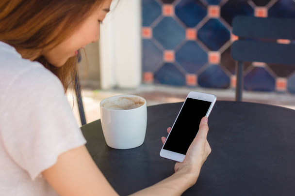 Молодая азиатка, использующая смартфон, маскирует чистый черный экран в кафе. Общение женщин в стиле жизни и работа в концепции кафе
. - Фото, изображение