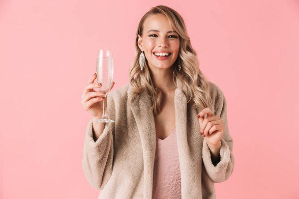 Emotional young pretty woman posing isolated over pink wall background holding glass with alcohol drink. - Foto, Imagen
