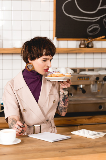 незадоволена бізнес-леді тримає тарілку з макарунами, стоячи за барною стійкою в кафетерії
 - Фото, зображення