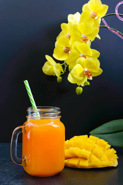 Mango smoothie bir cam kavanoz ve siyah bir zemin üzerine taze mango. Mango shake. Tropikal meyve kavramı. - Fotoğraf, Görsel