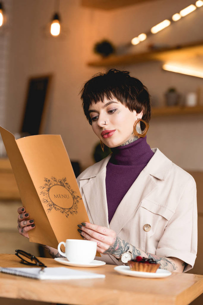 beautiful businesswoman holding menu while sitting at table in cafeteria - Photo, Image