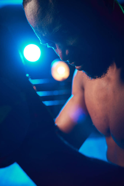 Close-up portrait of concentrated boxer on the ring. Studio shot, blue light. Light projectors behind man - Foto, immagini