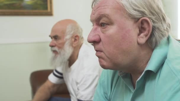 Close up of two mature senior men watching TV at home. Friends watching football soccer while eating chips. People involved in game - Кадри, відео