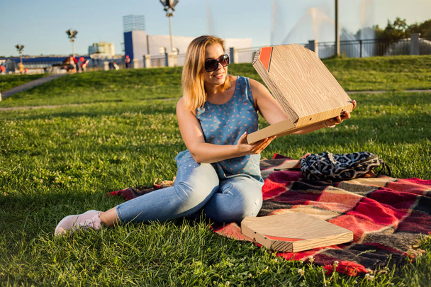 glückliche junge Frau hält heiße Pizza im Kasten, Sitz im Freien im Park - Foto, Bild