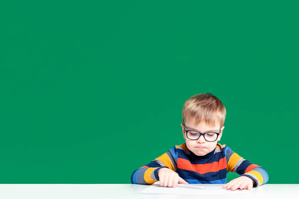 Offended boy with glasses sitting at a desk. Copy space - Foto, Imagem