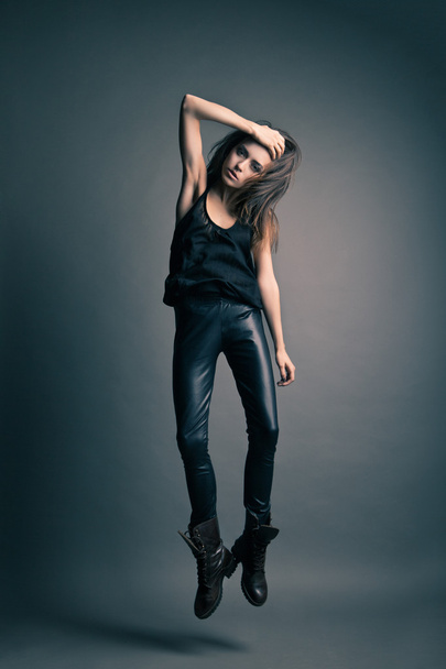 Fashion model wearing leather pants jump on grey - Photo, image