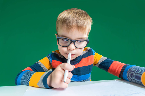 Zamyślony, mały chłopiec w okularach siedzi przy biurku, holdin - Zdjęcie, obraz