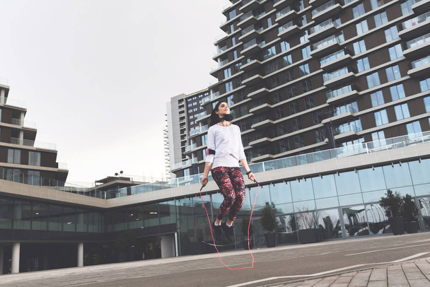 Attractive sporty young woman jumping the rope in front of urban modern buildings - Фото, зображення