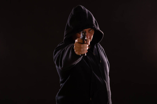 Man in black hoodie points pistol - Фото, изображение